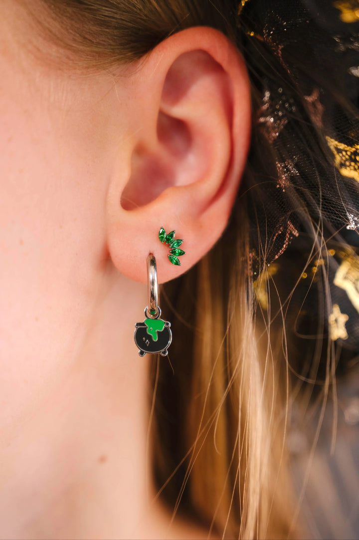Close-up of an ear wearing a black and green enamel cauldron hoop charm with a blurred background