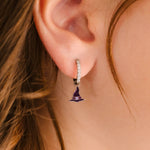 Close-up of an ear wearing a small purple witch hat charm hoop earring.