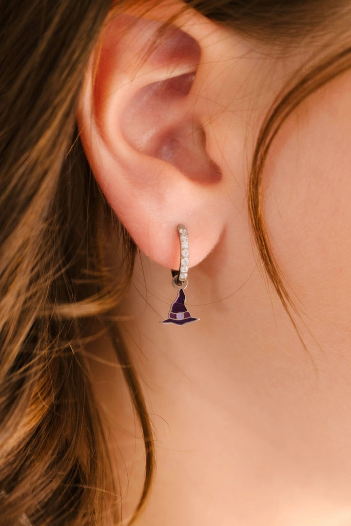 Close-up of an ear wearing a small purple witch hat charm hoop earring.