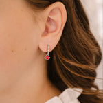 Close-up of an ear wearing a silver earring with a red enamel lips charm.