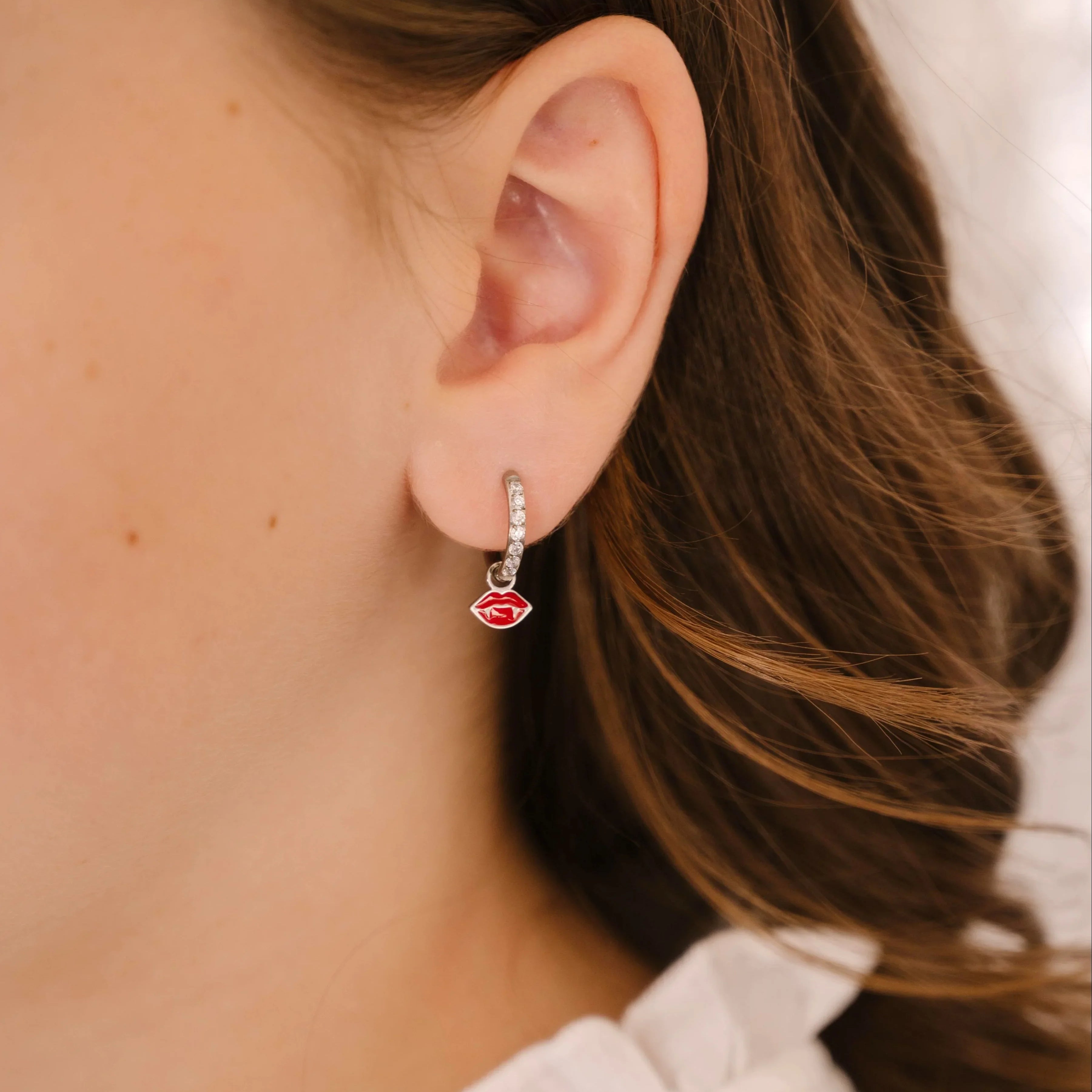 Close-up of an ear wearing a silver earring with a red enamel lips charm.