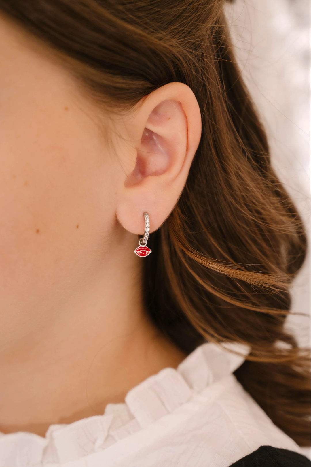 Close-up of an ear wearing a silver earring with a red enamel lips charm.