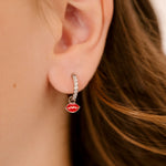 Close-up of an ear wearing a clear gem-studded hoop earring with a red enamel lip charm.