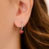 Close-up of an ear wearing a clear gem-studded hoop earring with a red enamel lip charm.