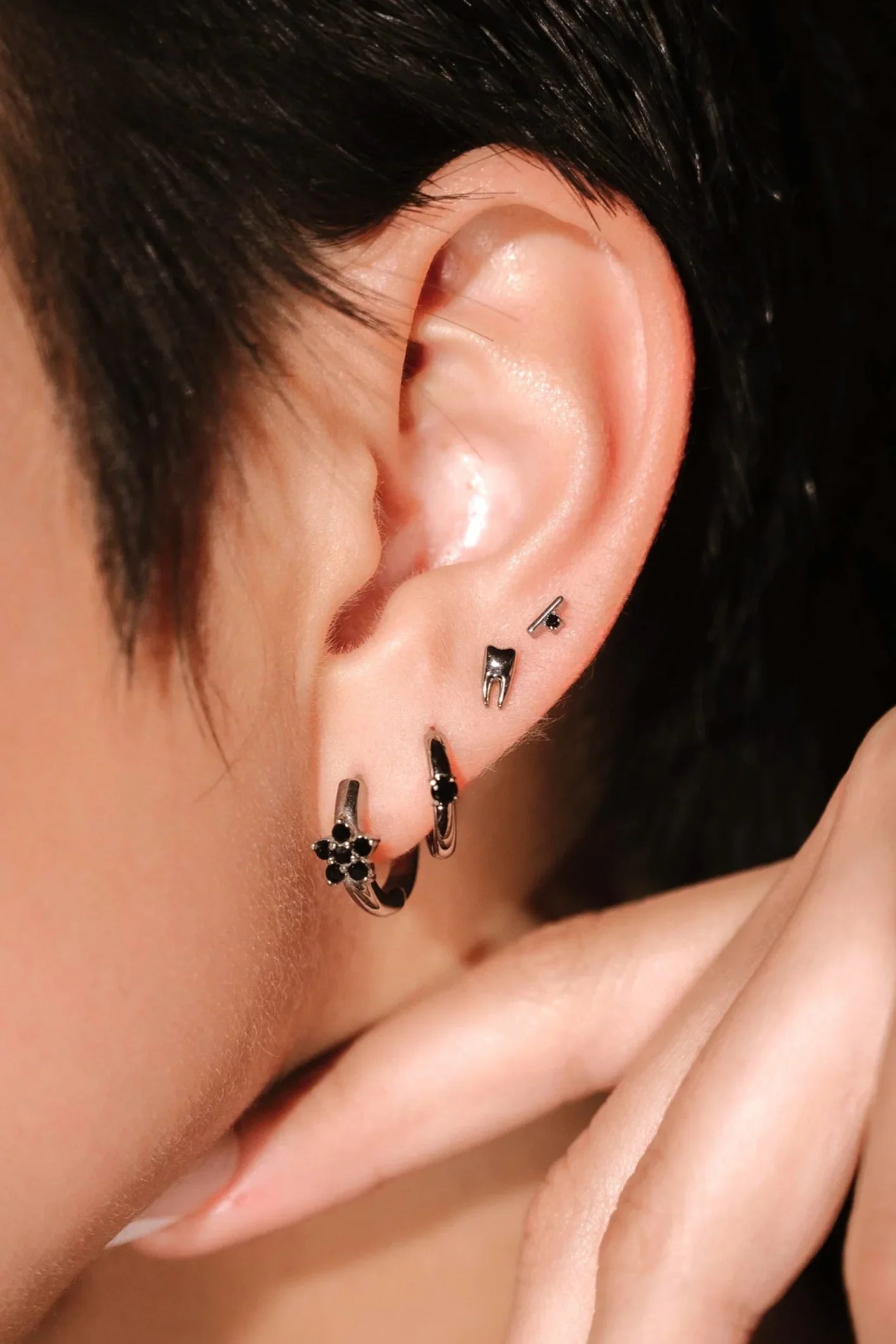 Close-up of an ear with a stack of several silver and black earrings against a neutral background