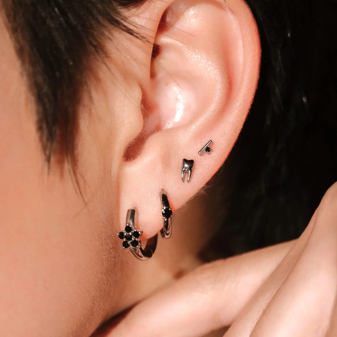 Close-up of an ear with a stack of several silver and black earrings against a neutral background