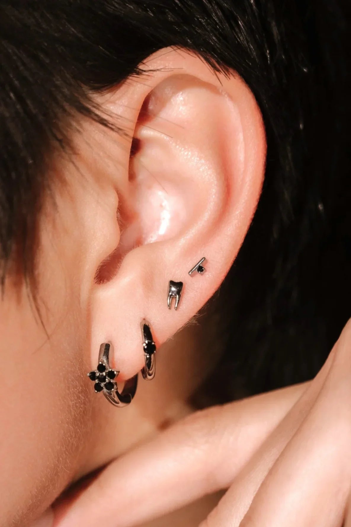 Close-up of an ear with a several silver and black earrings against a neutral background
