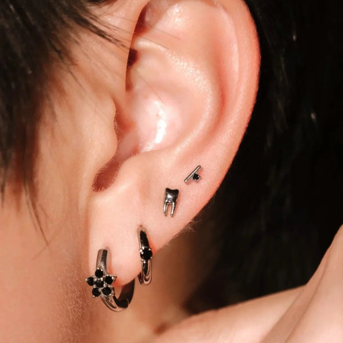 Close-up of an ear with a several silver and black earrings against a neutral background