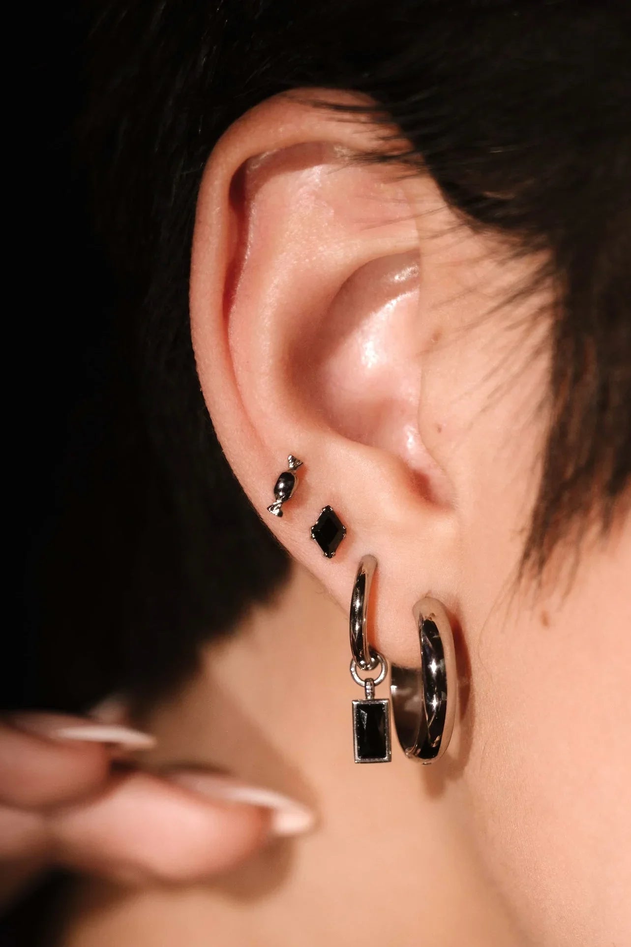 close up photo of an ear wearing black and silver earrings