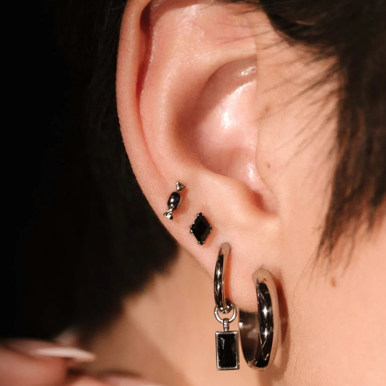 close up photo of an ear wearing black and silver earrings