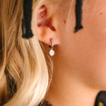 Close-up of an ear wearing a silver hoop with silver and white skull charm on a blurred background