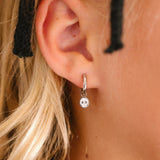 Close-up of an ear wearing a silver hoop with silver and white skull charm on a blurred background