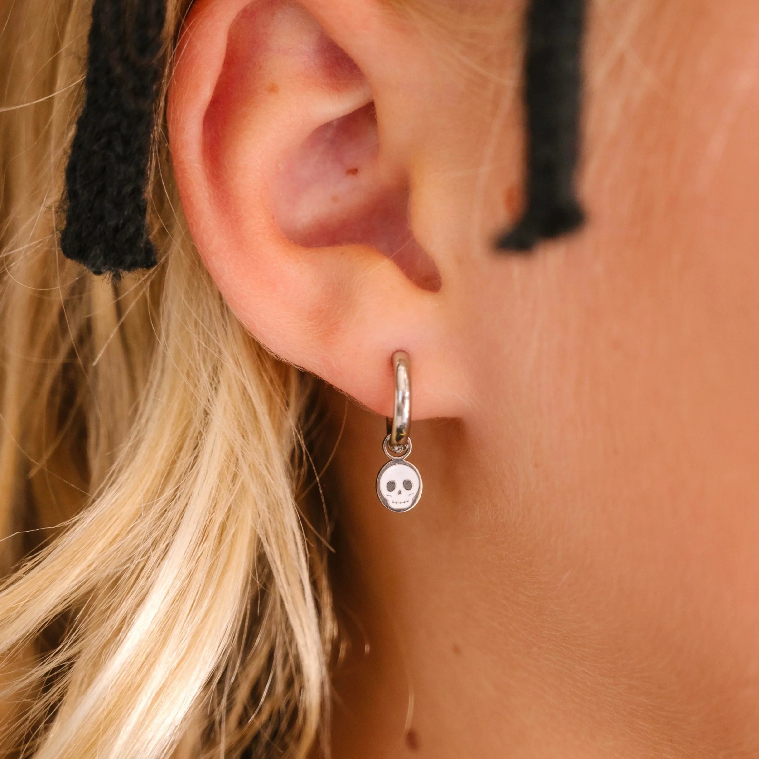 Close-up of an ear wearing a silver hoop with silver and white skull charm on a blurred background