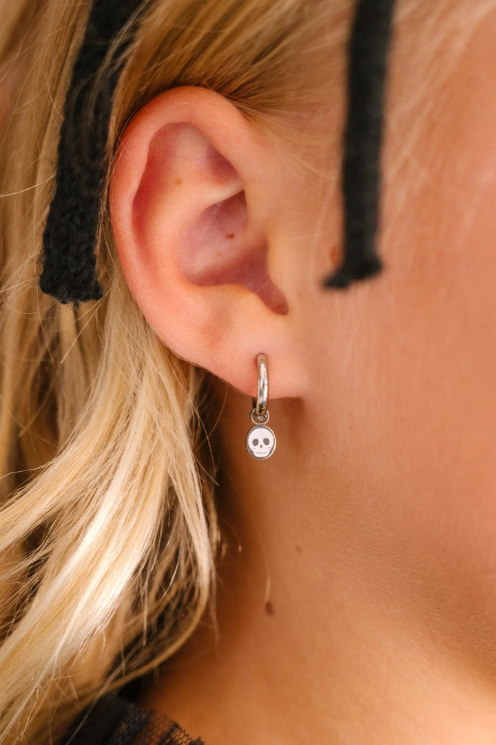 Close-up of an ear wearing a silver hoop with silver and white skull charm on a blurred background