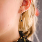 Close-up of a a person with blonde hair, wearing a silver hoop that has a dangling black and silver spider charm hanging on a chain.