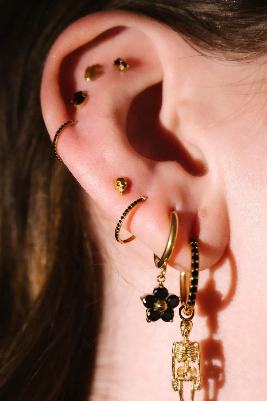 Close up photo of an ear wearing gold and black flat backs and hoops