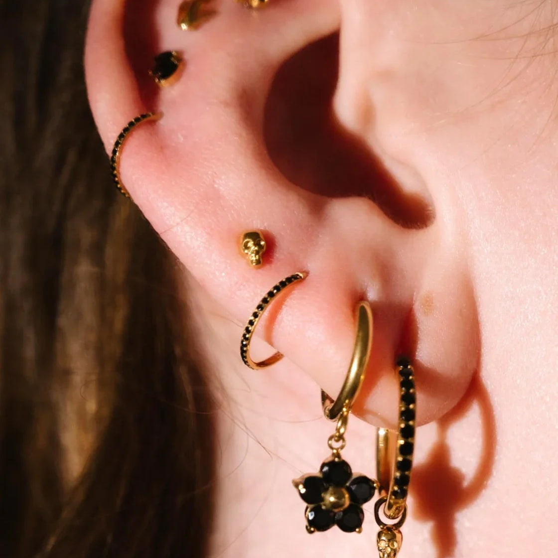 Close up photo of an ear wearing gold and black flat backs and hoops