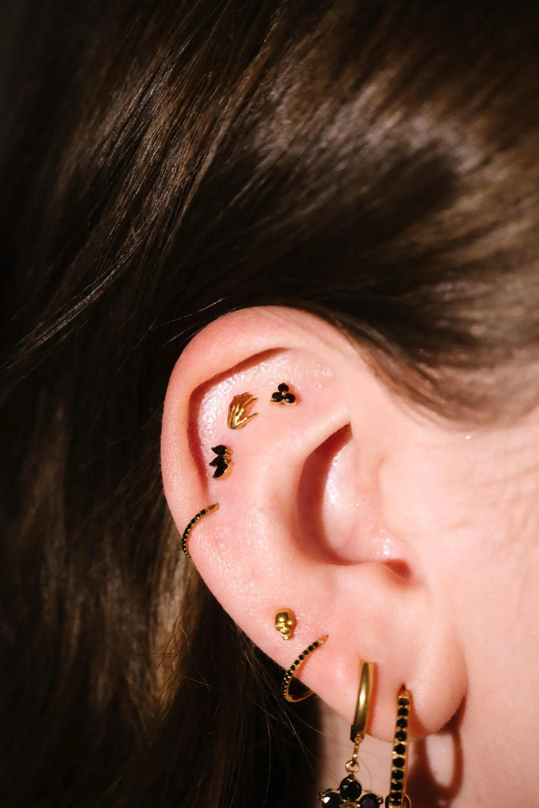 Close up of an ear with black and gold flat backs and hoops