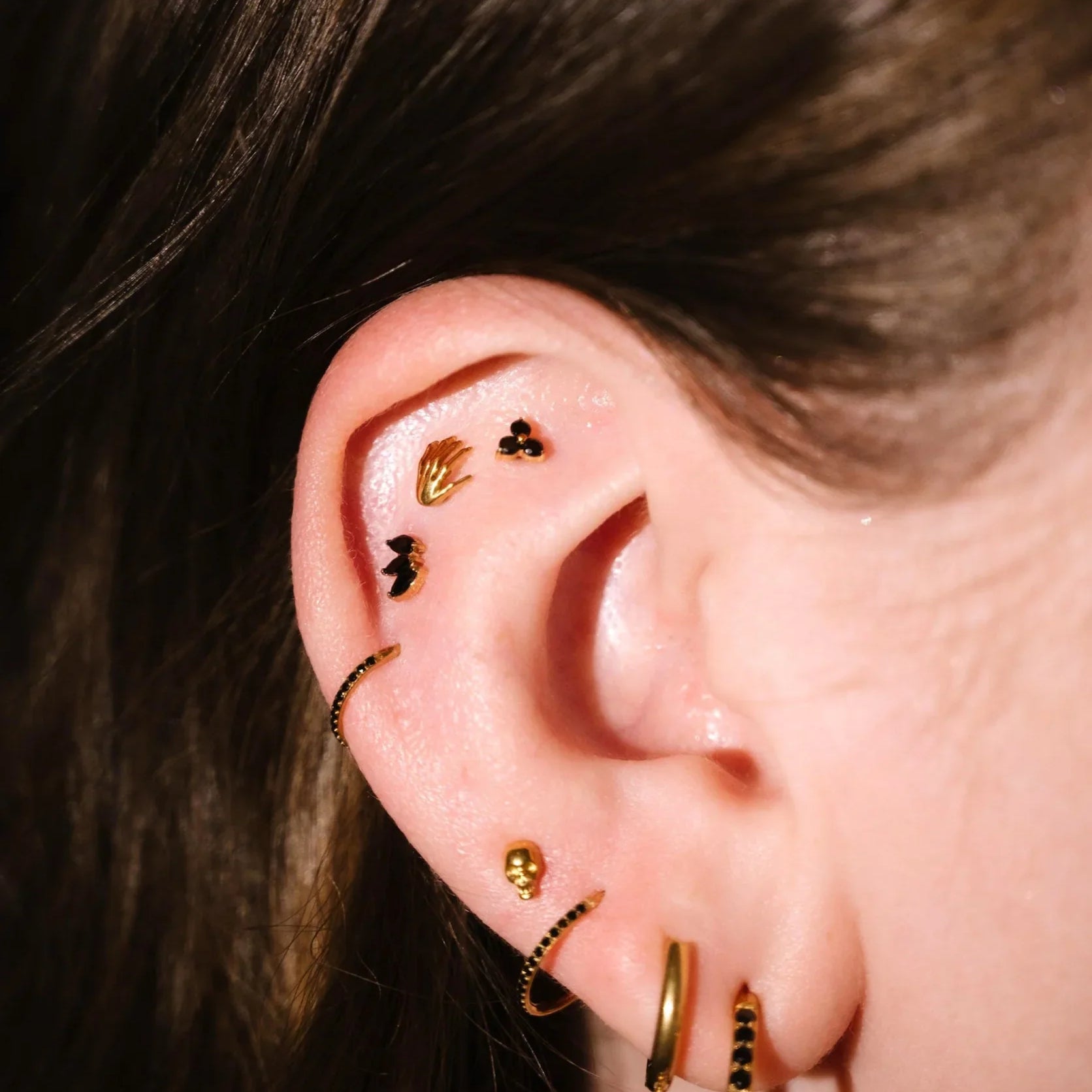 Close up of an ear with black and gold flat backs and hoops