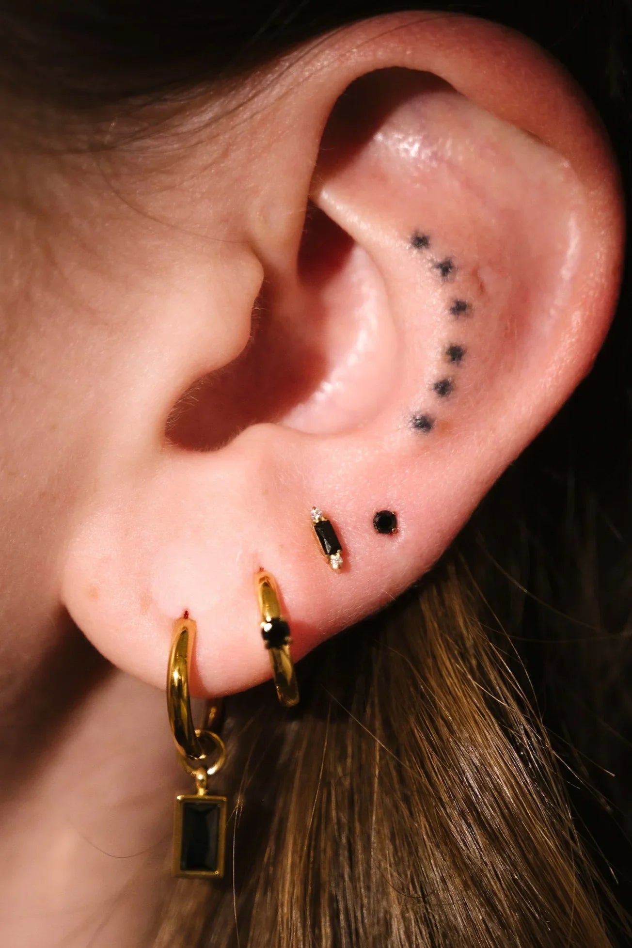 Close up of an ear with black and gold flat backs and hoops