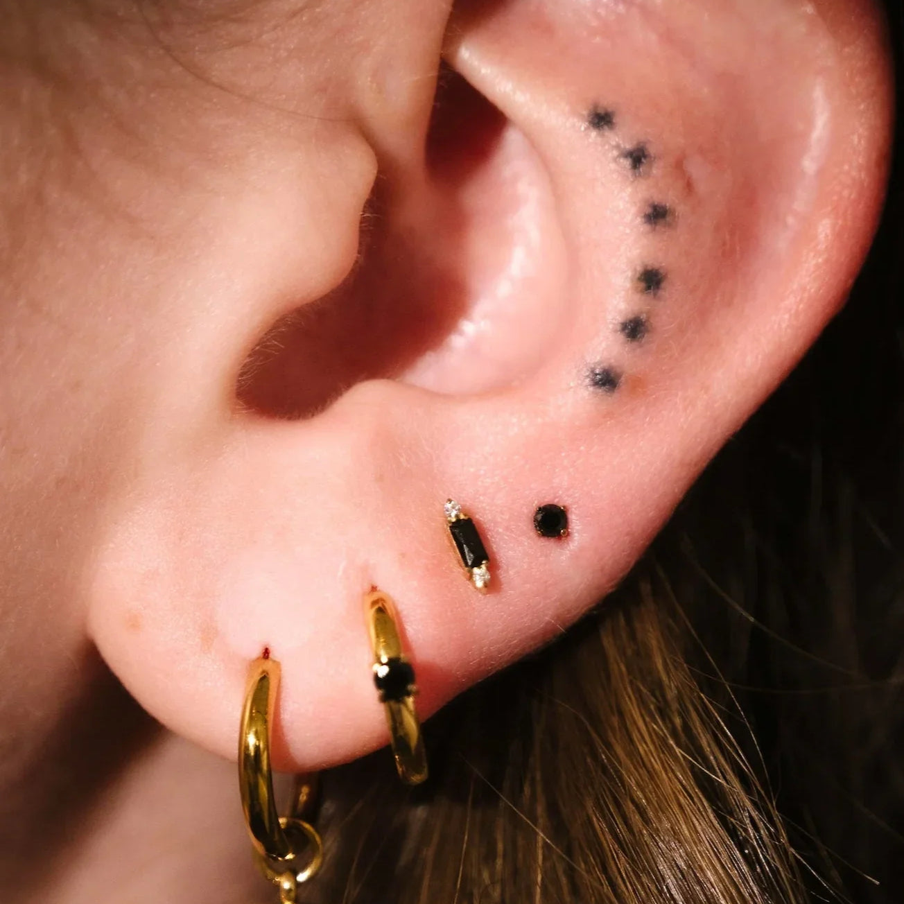Close up of an ear with black and gold flat backs and hoops