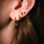 Close-up of an ear with gold hoop earrings and black studs.