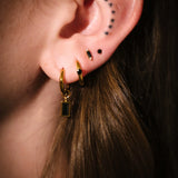 Close-up of an ear with gold hoop earrings and black studs.