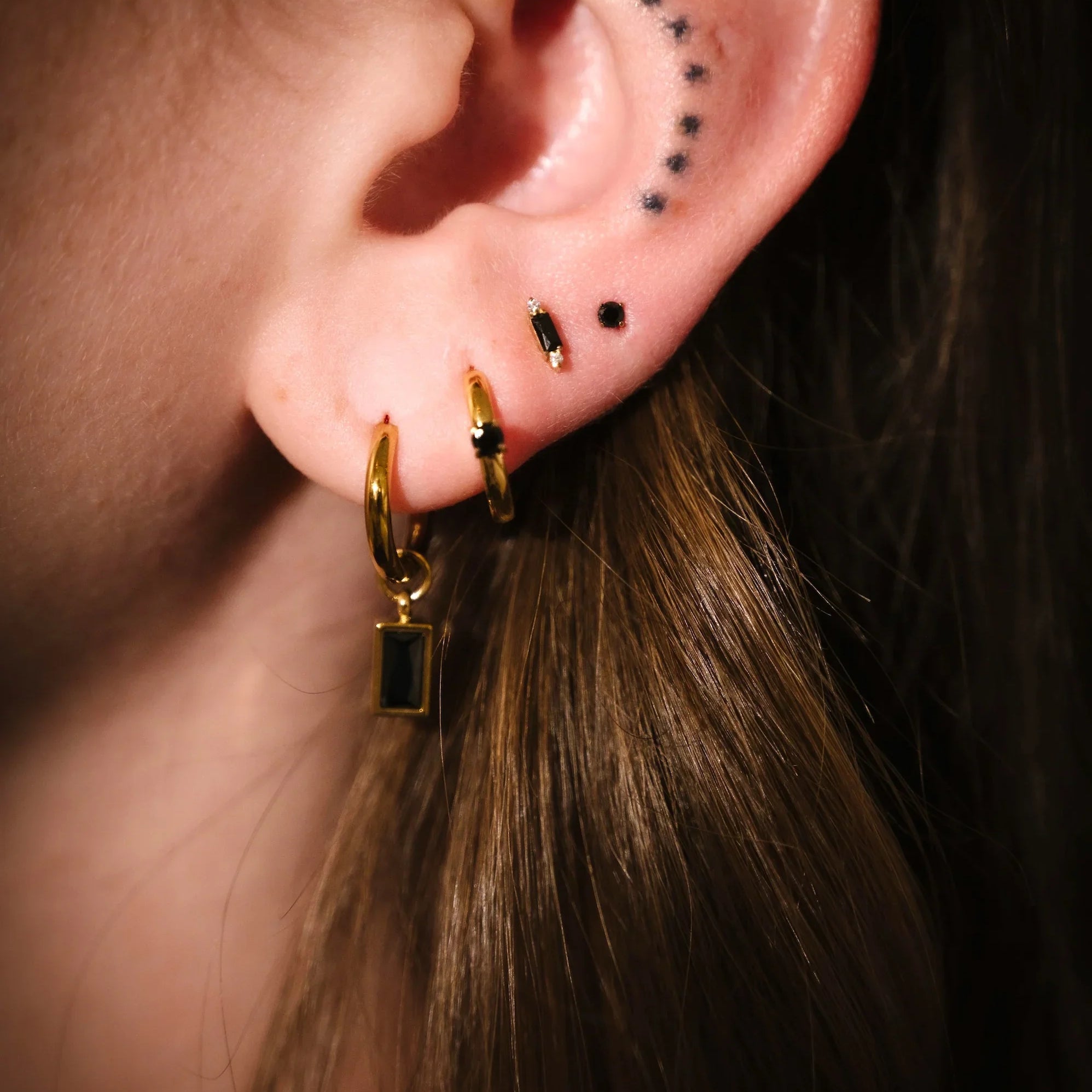 Close-up of an ear with gold hoop earrings and black studs.