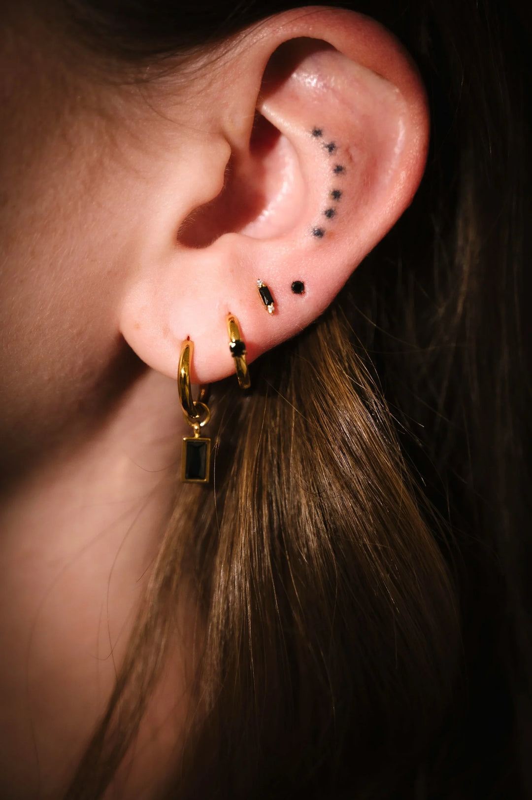 Close-up of an ear with gold hoop earrings and black studs.