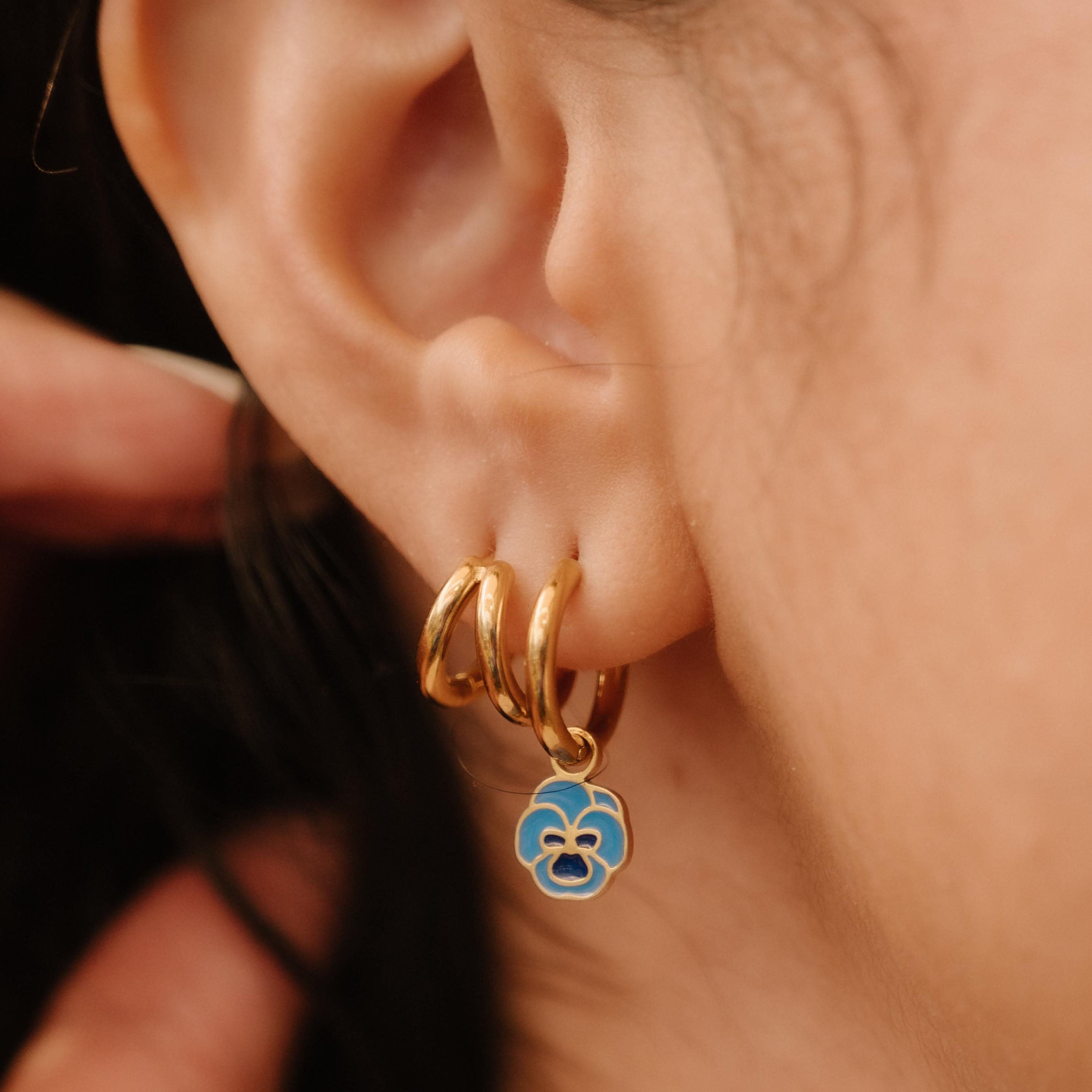Close-up of an ear wearing gold hoop earrings with a blue enamel flower charm.
