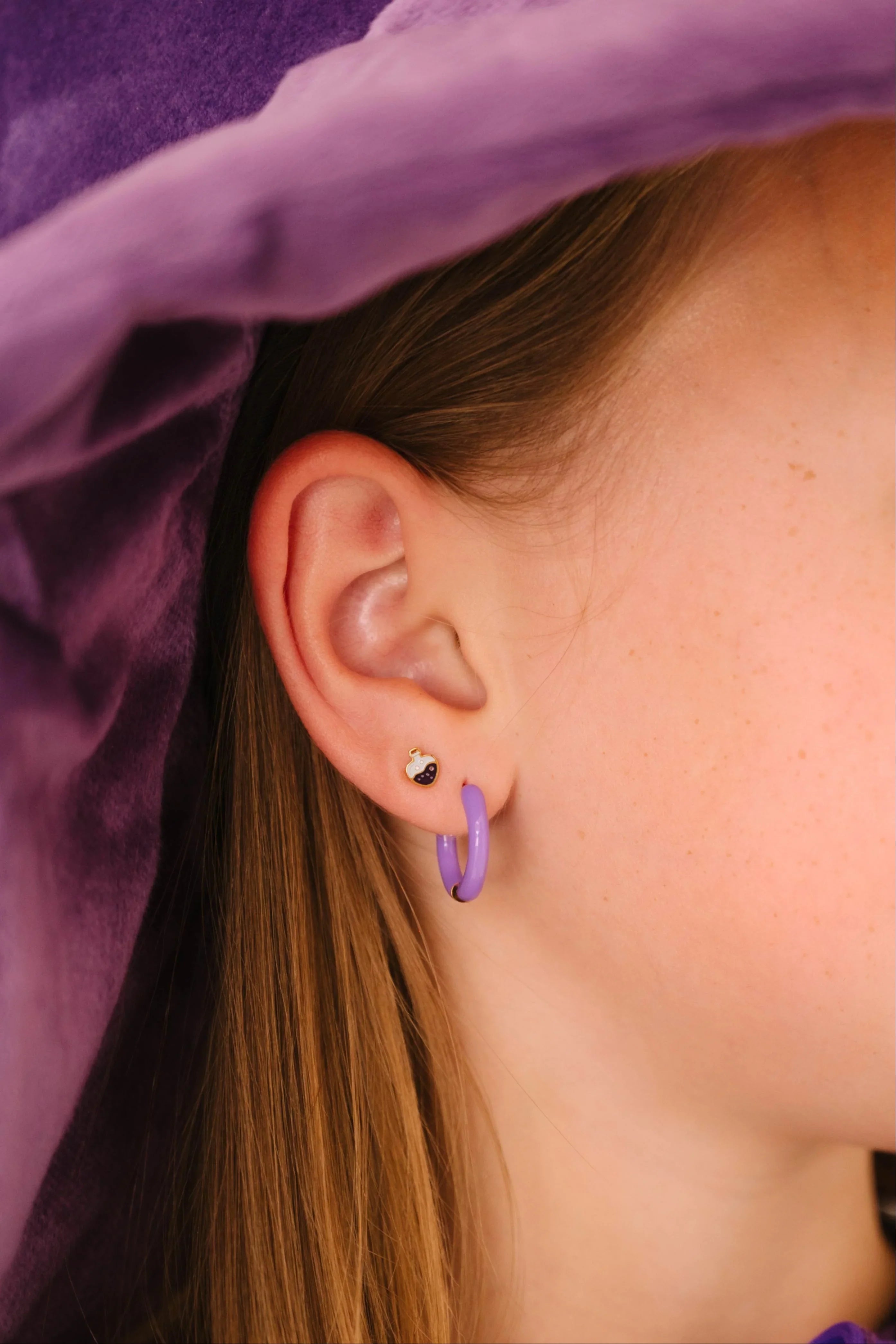 Close-up of a child wearing a purple witch hat and outfit, with a focus on a purple enamel potion bottle-shaped stud earring.