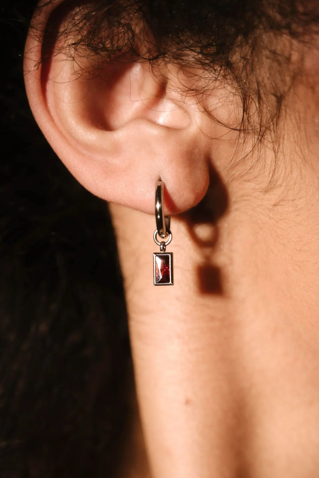 Close up of an ear with a hoop and garnet charm 
