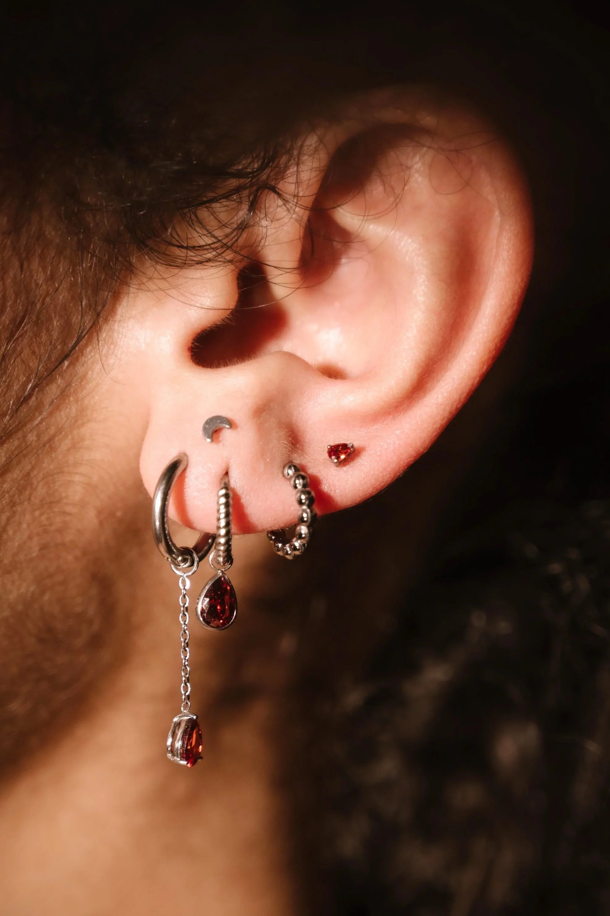 Close-up of an ear with multiple earrings against a dark background