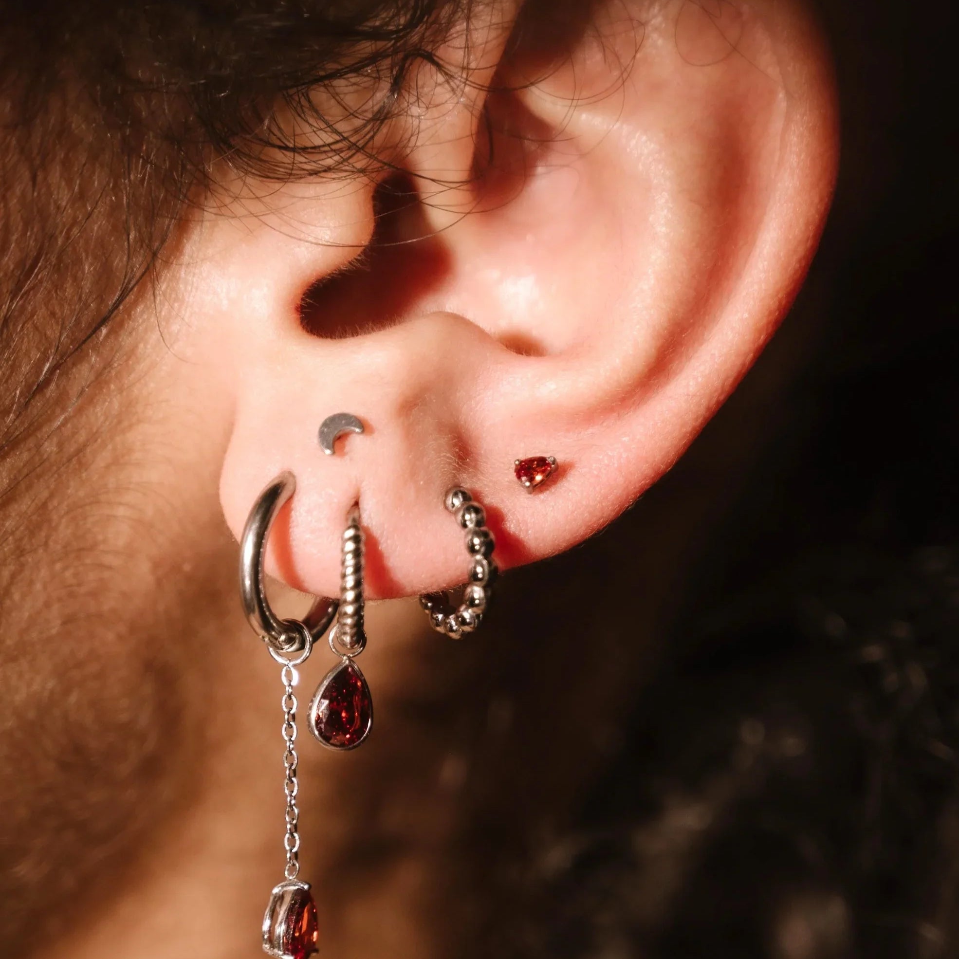Close-up of an ear with multiple earrings against a dark background