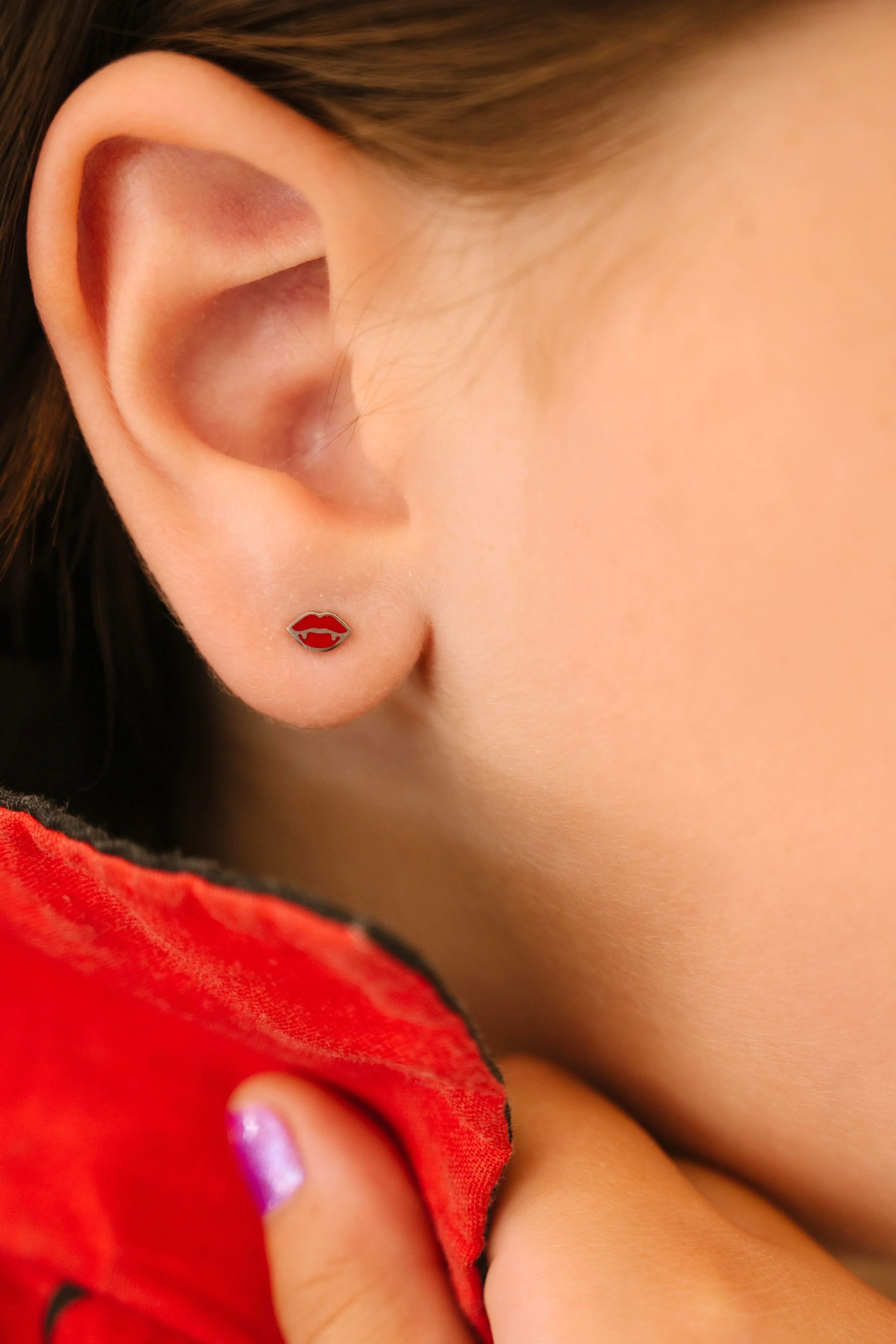 Close-up of an ear wearing a red lips earring with a blurred background