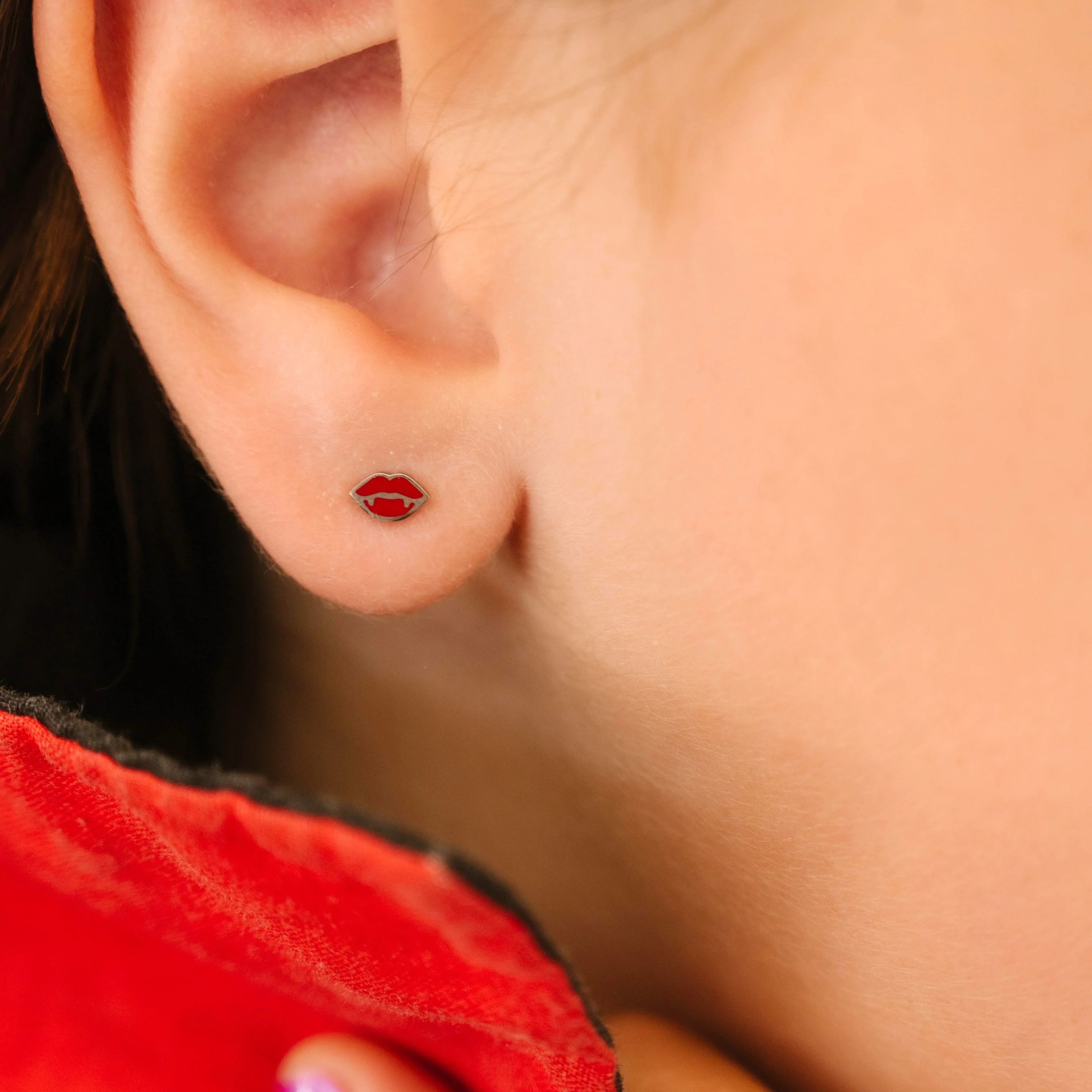 Close-up of an ear wearing a red lips earring with a blurred background