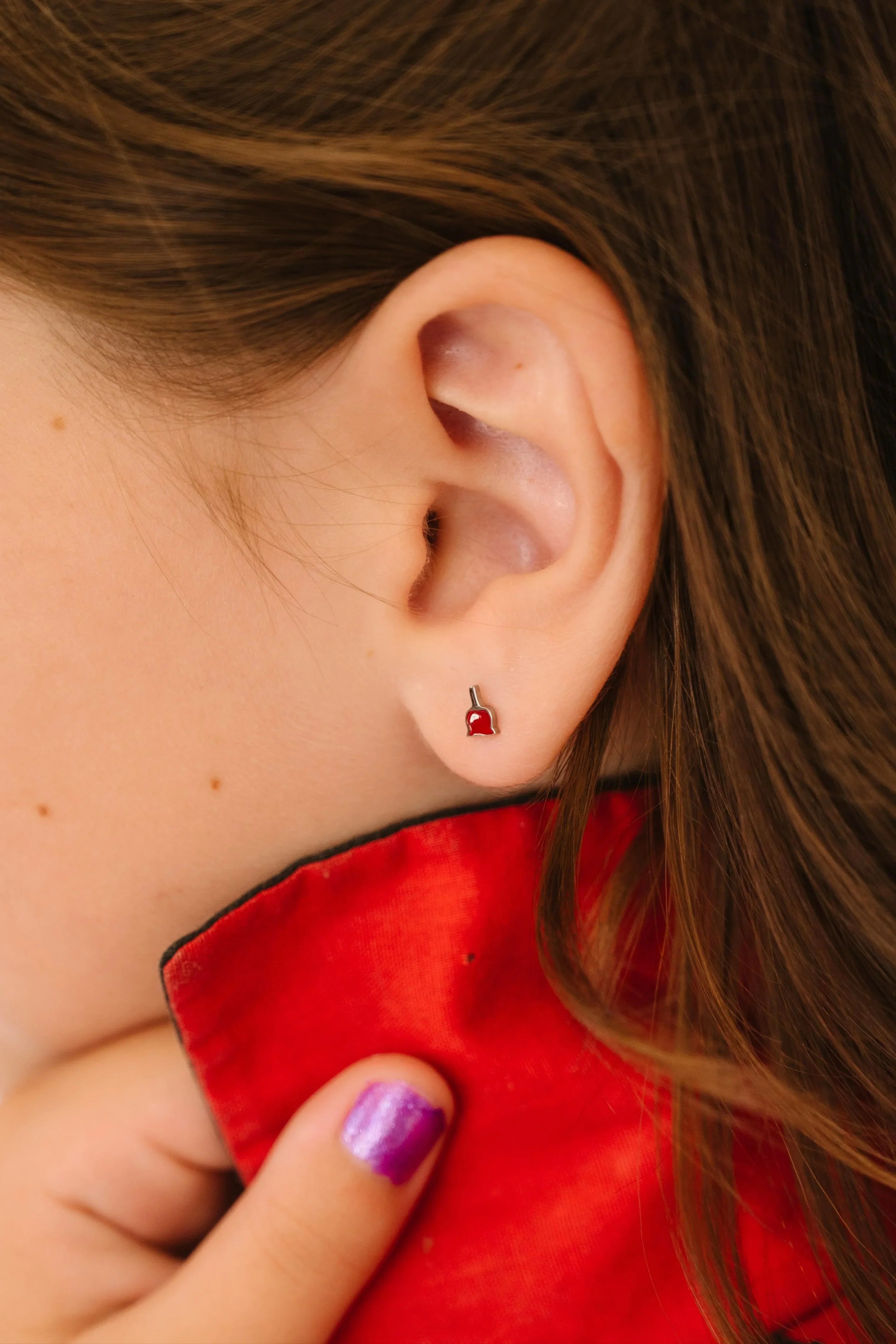 Close-up of a child wearing a red earring with a small dipped candy apple design.
