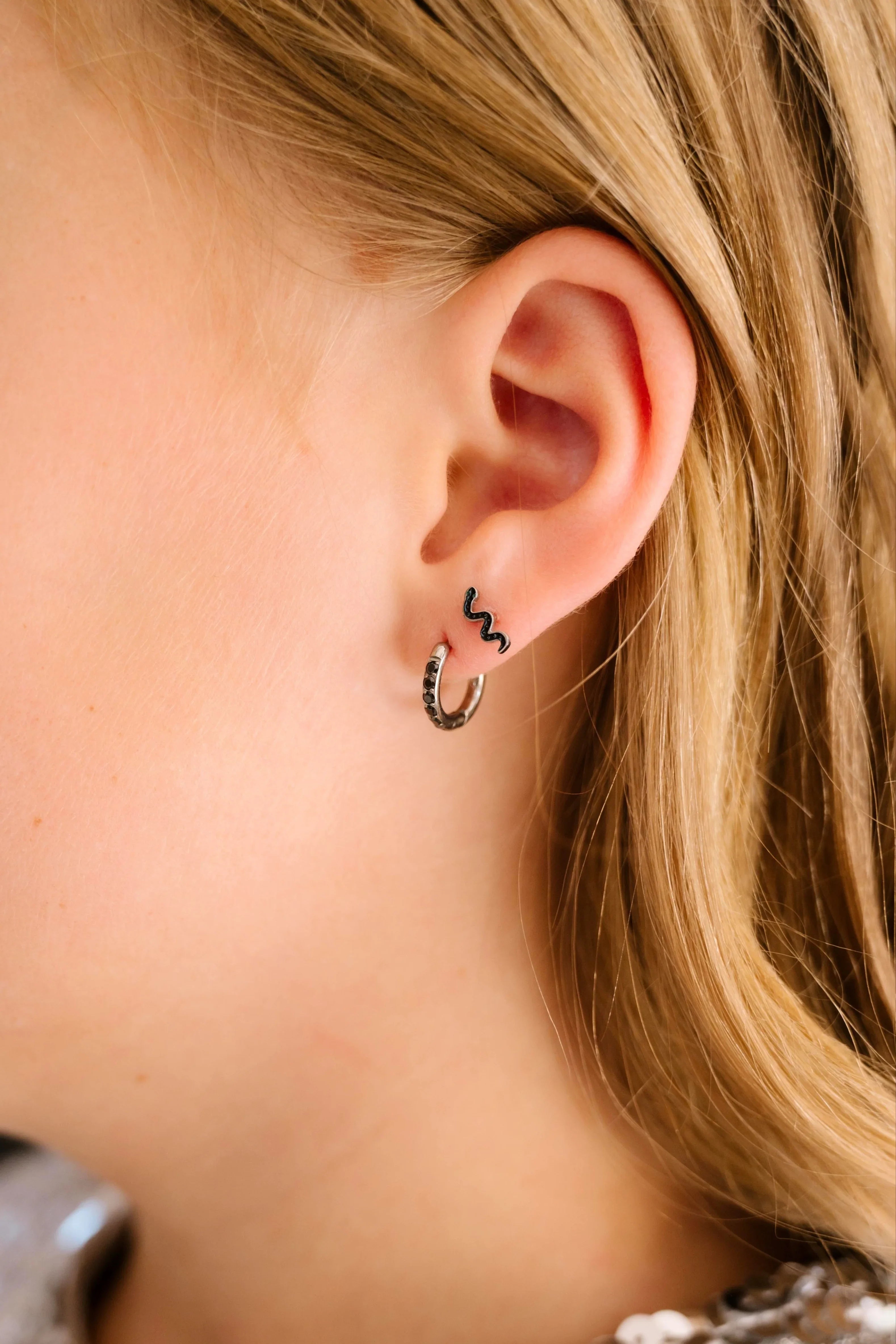 Close-up of a person wearing a squiggle snake earring with a blurred background