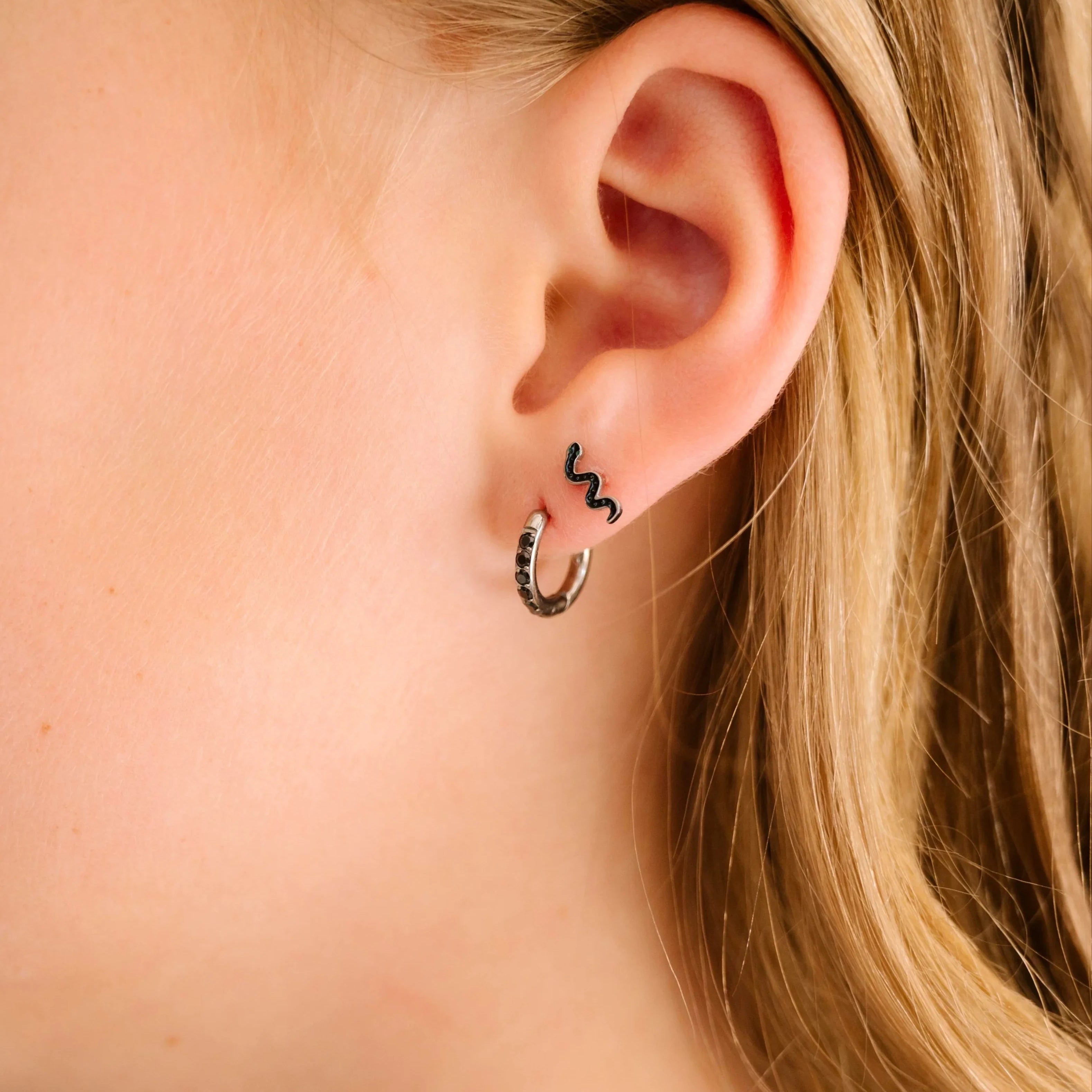 Close-up of a person wearing a squiggle snake earring with a blurred background