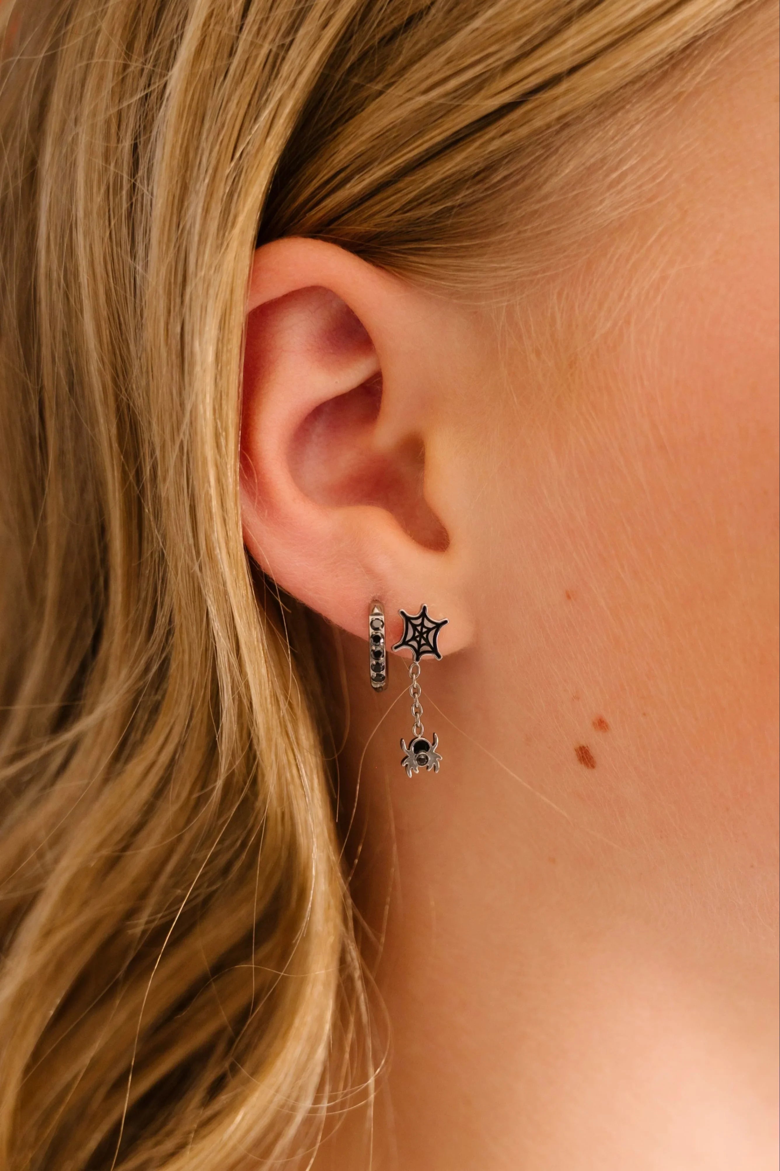 Close-up of an ear wearing spiderweb and spider dangle stud earring with a blurred background