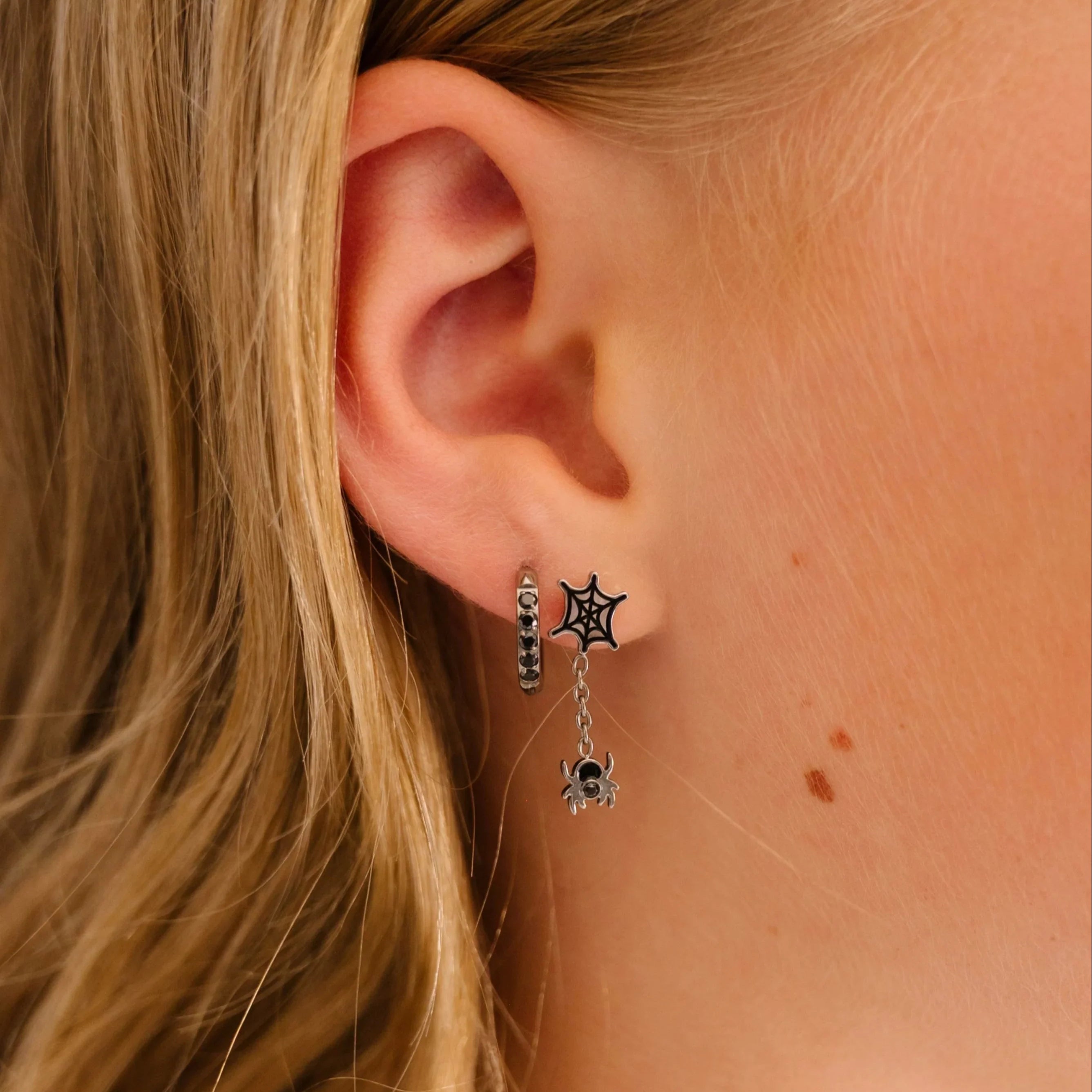 Close-up of an ear wearing spiderweb and spider dangle stud earring with a blurred background