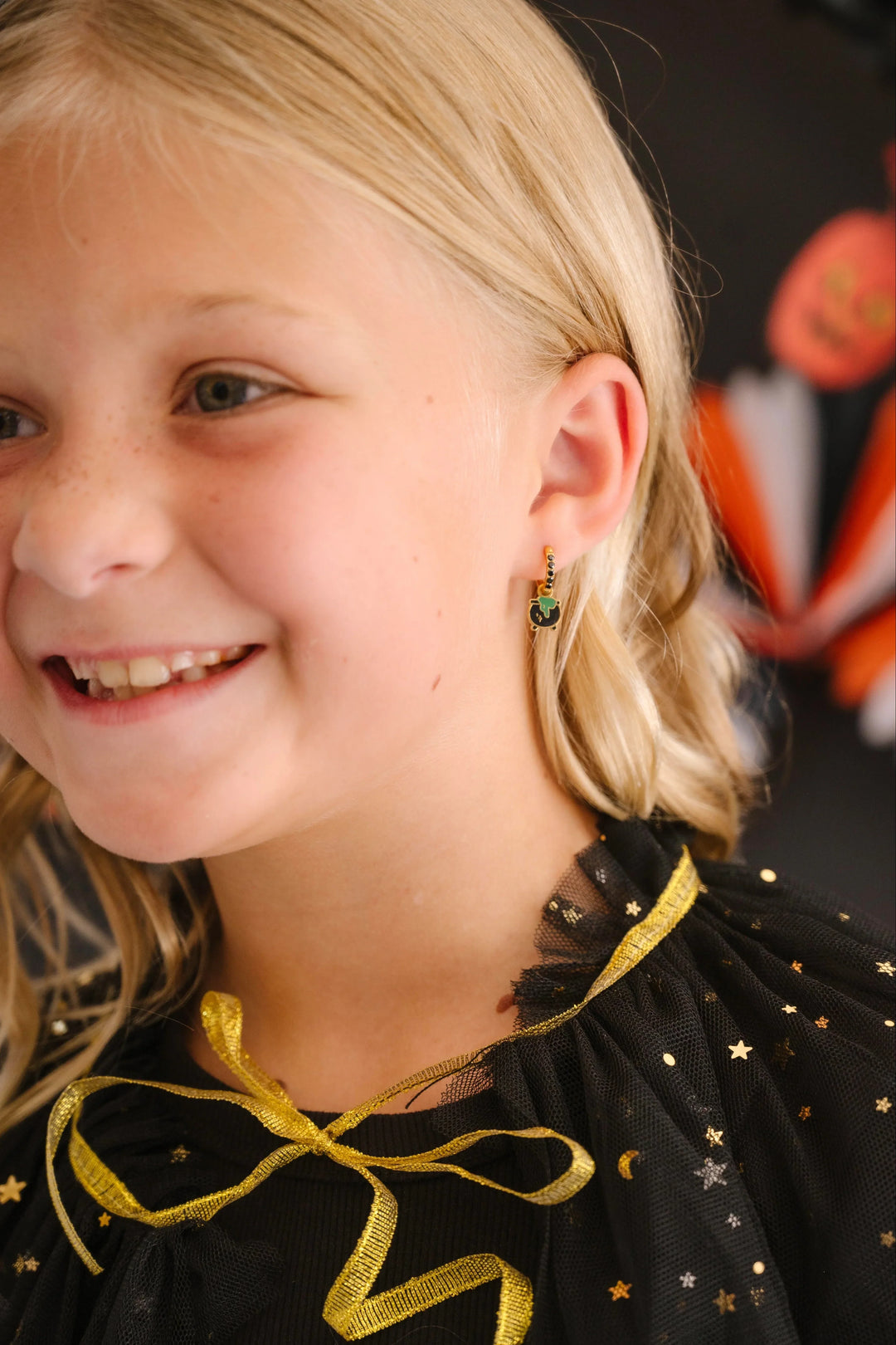 Girl with blonde hair wearing a black dress with gold accents, smiling.