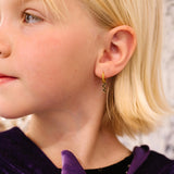 Close-up of a child wearing a gold hoop with a black squiggle snake charm with a blurred background