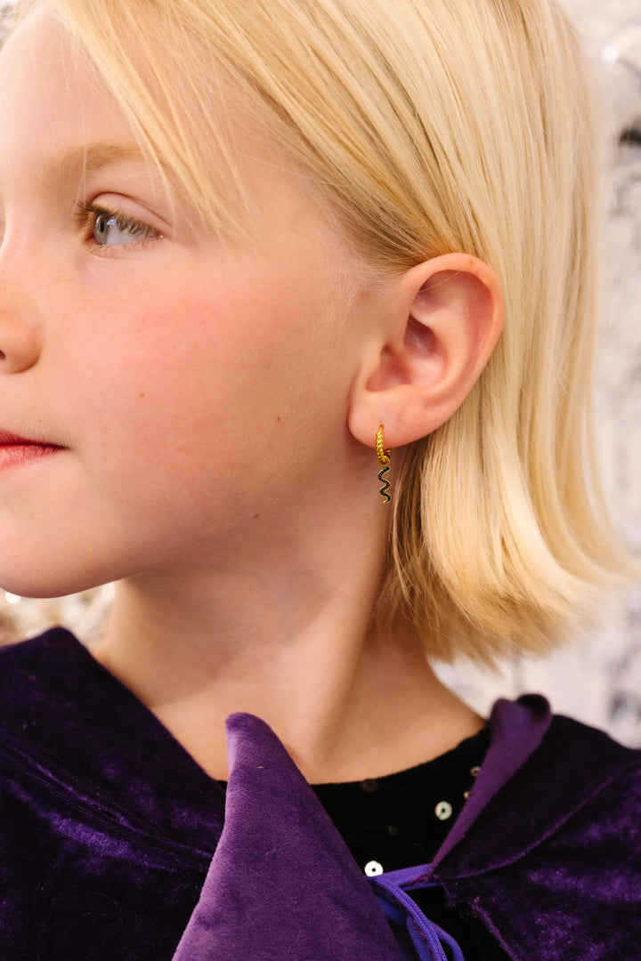 Close-up of a child wearing a gold hoop with a black squiggle snake charm with a blurred background