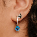 Close-up of an ear wearing silver hoop earrings with a blue enamel flower charm.