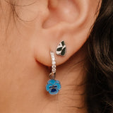 Close-up of an ear wearing silver hoop earrings with a blue enamel flower charm.