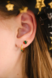 Close-up of an ear wearing gold earrings with green and red enamel, against a dark background with star patterns.