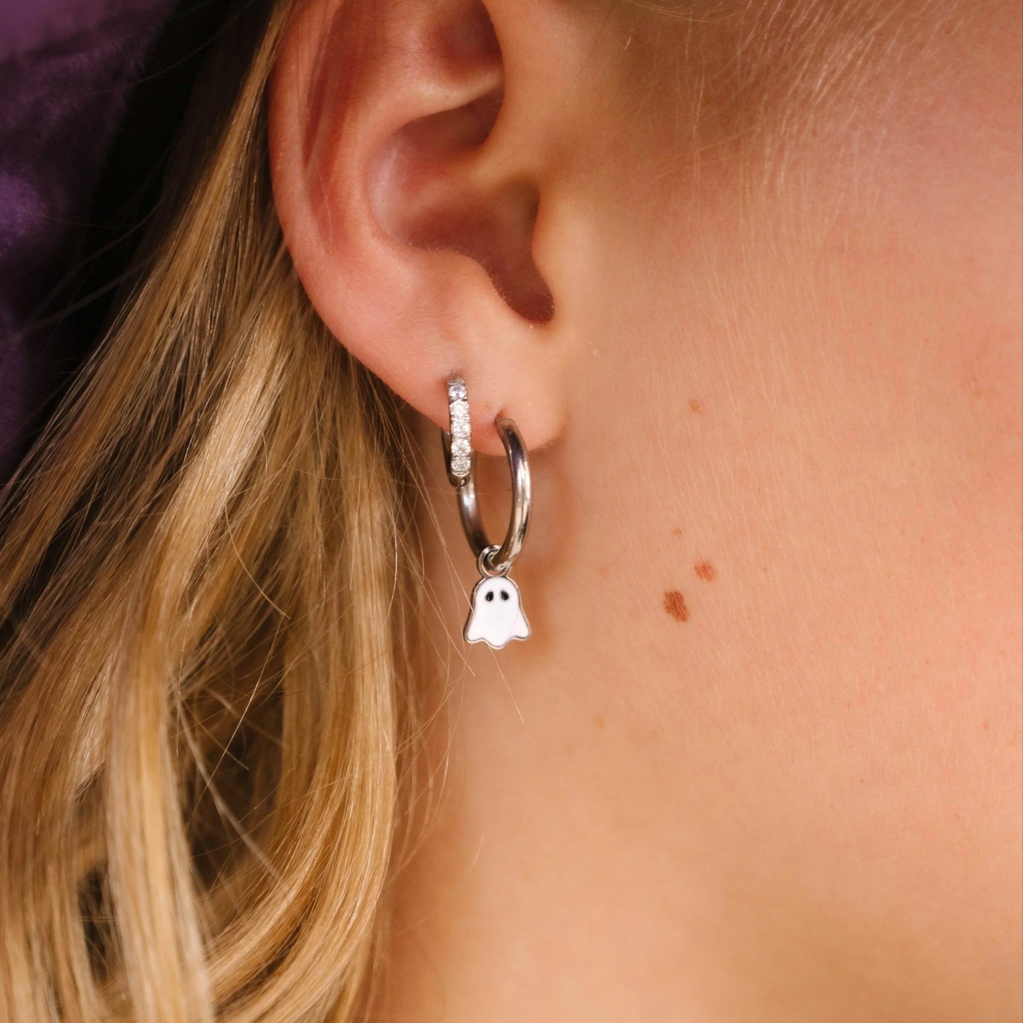 Close-up of a person wearing a silver hoop earring with a ghost charm.