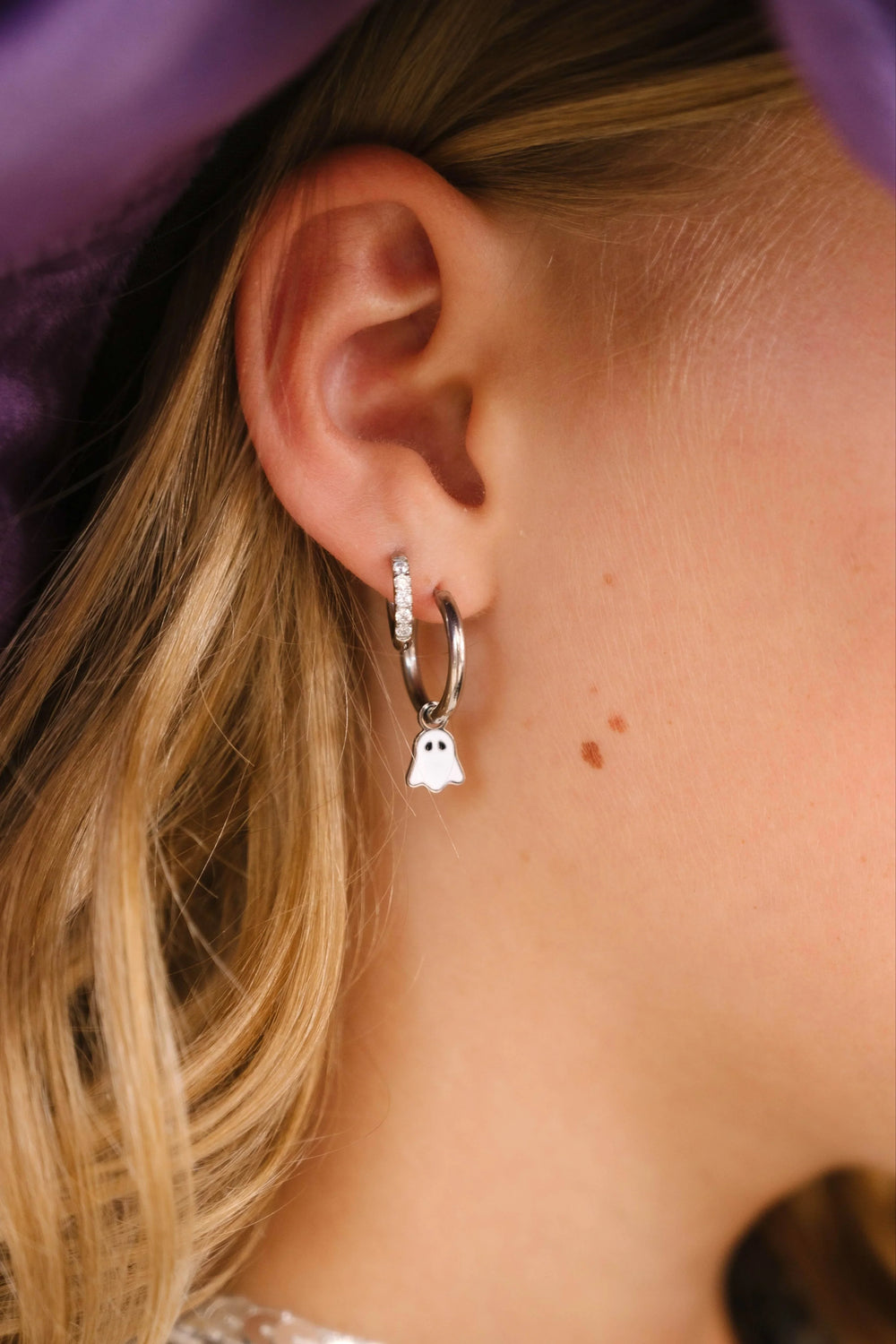 Close-up of a person wearing a silver hoop earring with a ghost charm.