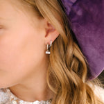Close-up of a person wearing a small earring with a purple velvet background